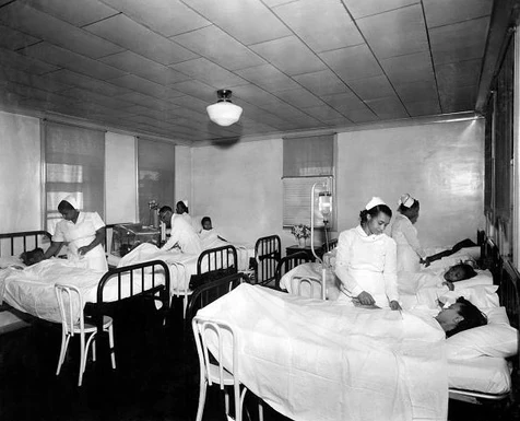 Historic hospital ward with women in beds and medical staff