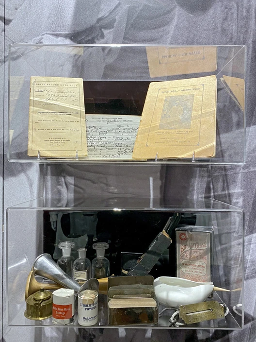 Museum display containing a midwife bag, bottles, dressings, and medical supplies