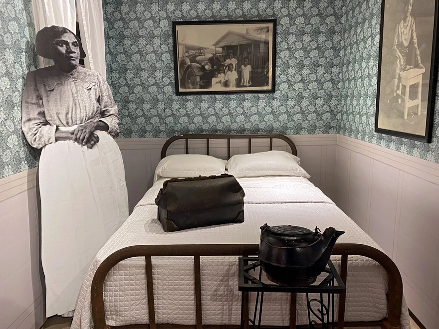 Interpretive domestic room with a bed, a standing midwife figure, and a medical bag